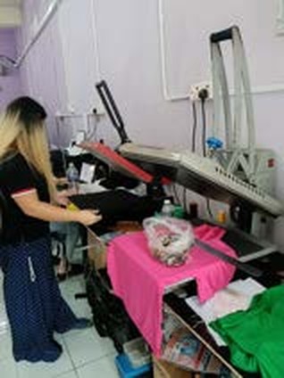 Pekerja menggunakan mesin heat press pada baju